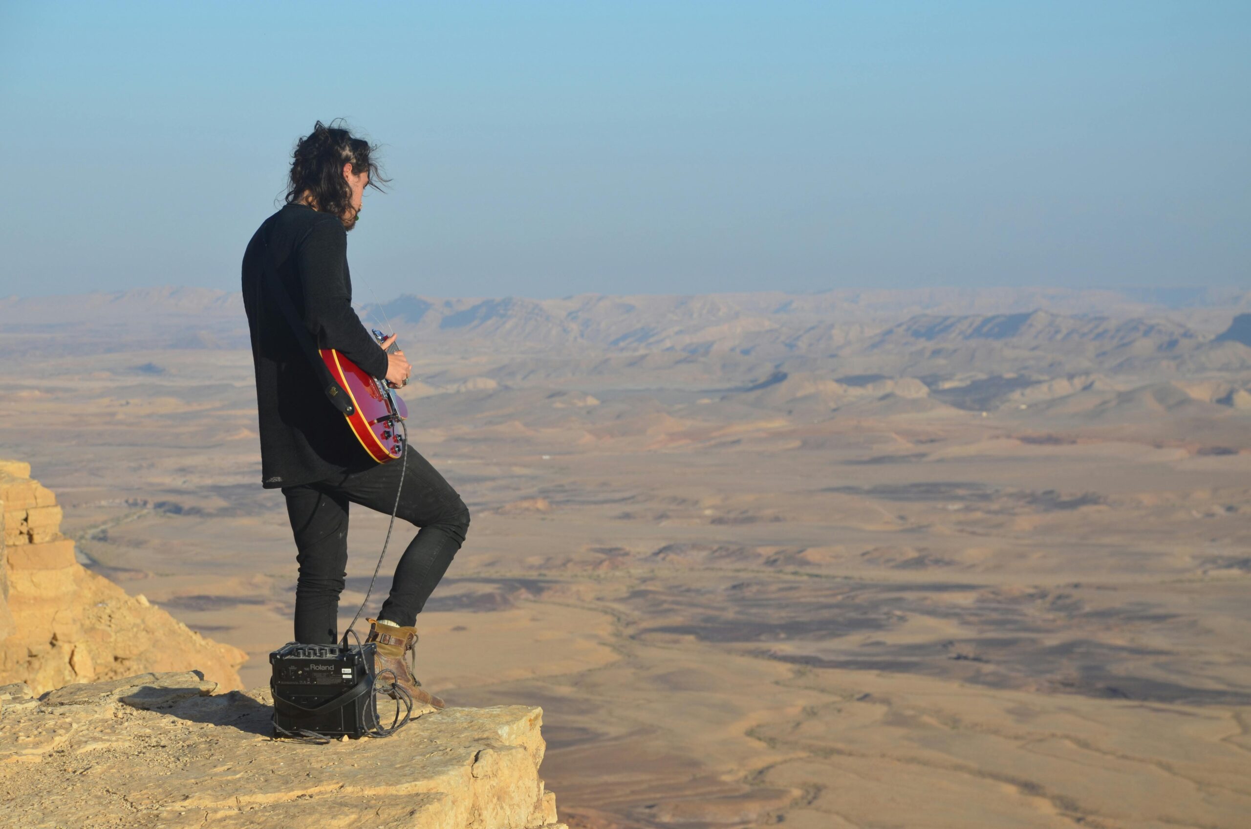Guitarist playing an electric guitar through a mini-amp on a mountain top.