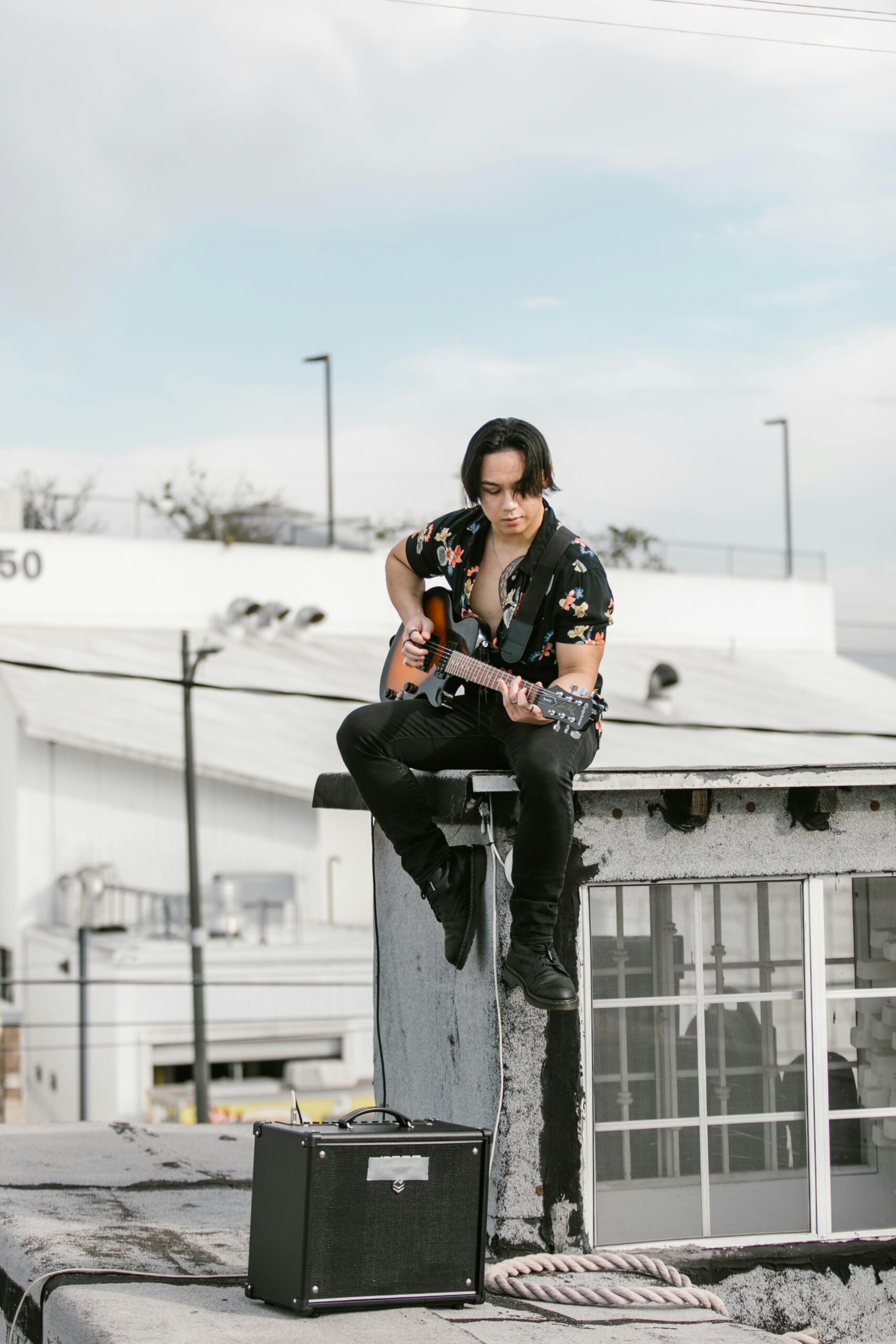 Guitarist playing electric guitar through a min-amp on a rooftop.